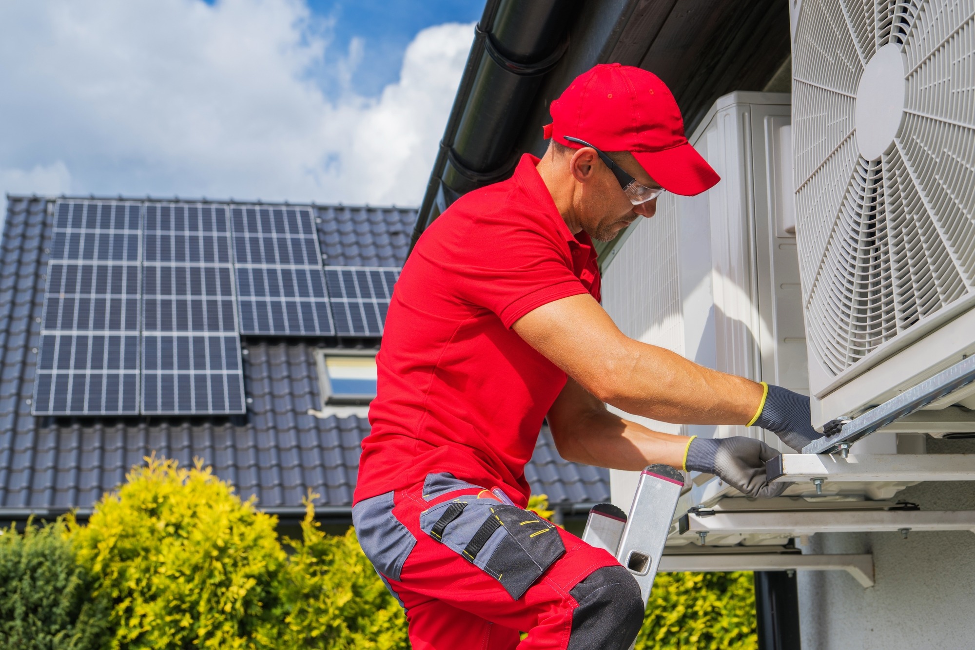 Technician performing heating repair Owosso on an outdoor HVAC unit beside a home.